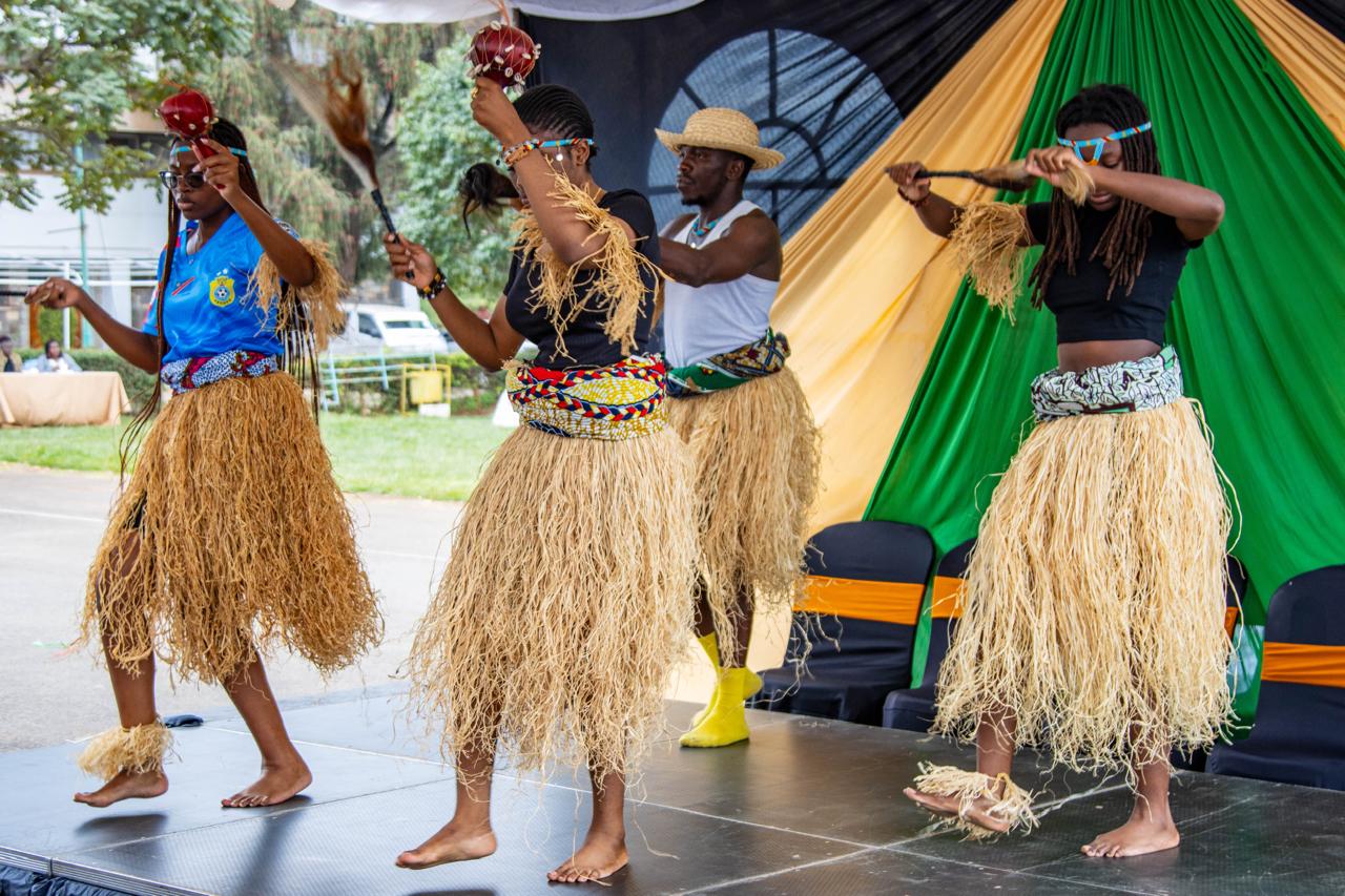 Four performers dancing on stage in raffia costumes while holding traditional instruments