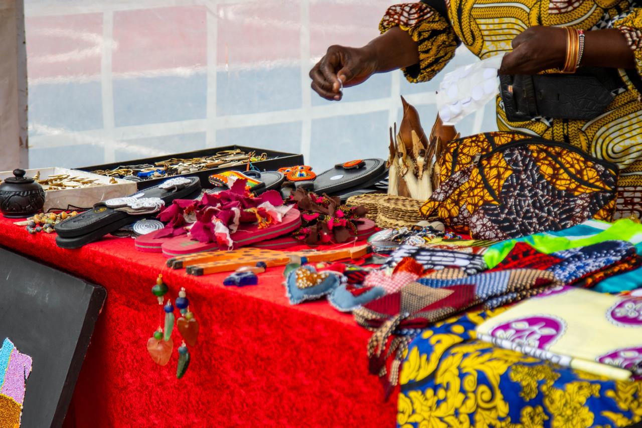 A vendor presenting handmade jewellery, sandals, textiles, accessories and woven craft items on a market table