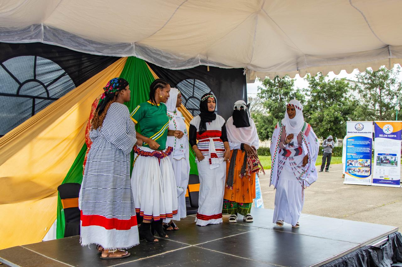 A multicultural group of women performing together on an outdoor stage in varied traditional clothing