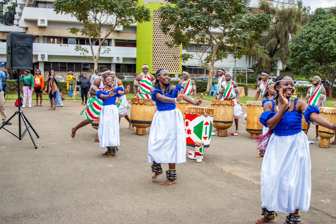 Dancers in blue and white performing in front of a large drumming ensemble at an outdoor celebration