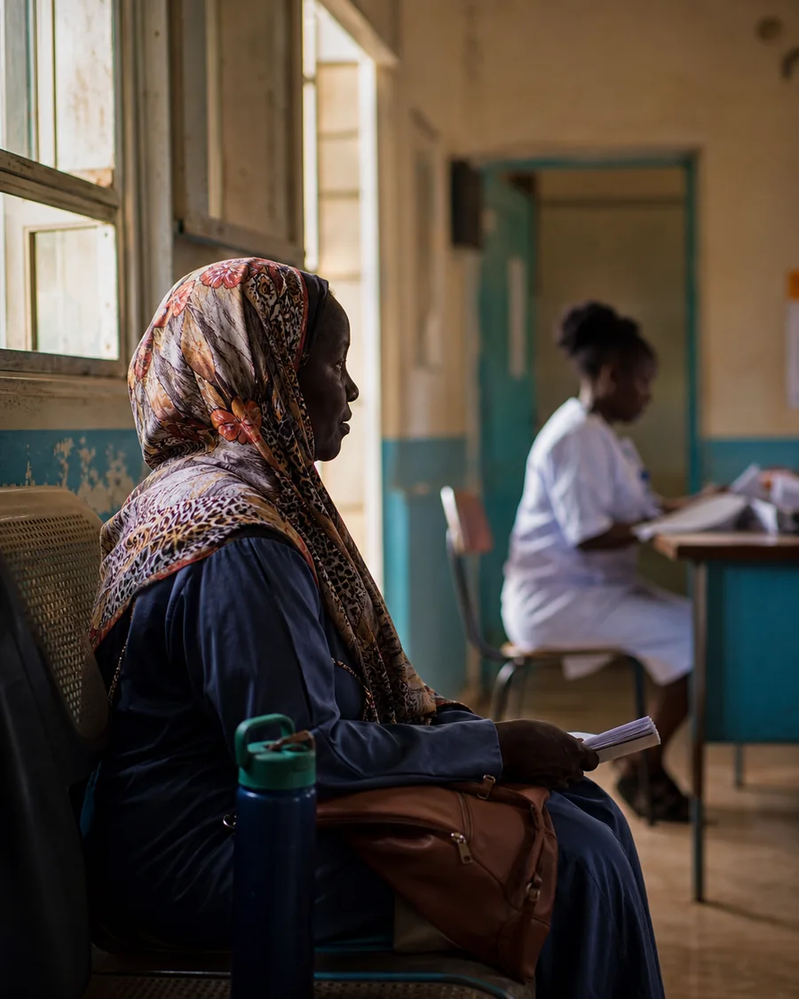 A woman waiting at a public clinic while a healthcare worker reviews papers nearby